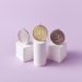 Gold, silver, and bronze medals displayed on white pedestals with a pink background.