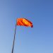 Red national flag of Kyrgyzstan waving on a flagpole under a clear blue sky.