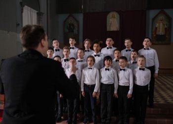 Boys choir in uniform singing under conductor's guidance in a church setting.