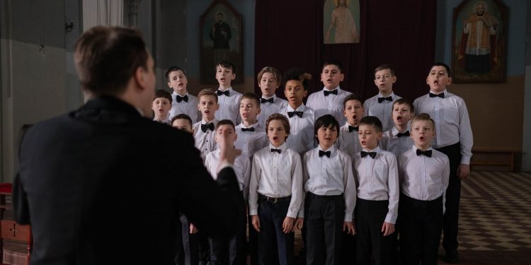 Boys choir in uniform singing under conductor's guidance in a church setting.