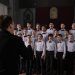 Boys choir in uniform singing under conductor's guidance in a church setting.