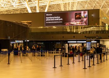 Travelers check in at Zagreb Airport with large advertising screen above.