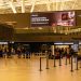 Travelers check in at Zagreb Airport with large advertising screen above.