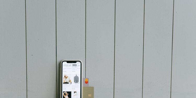 A smartphone displaying an ecommerce site with a credit card, set on a wooden surface, depicting online shopping.