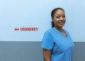 Happy healthcare worker in scrubs standing near emergency room sign.