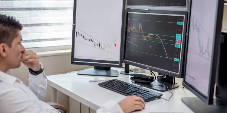 Business professional analyzing financial data on multiple computer monitors at his workspace.
