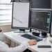 Business professional analyzing financial data on multiple computer monitors at his workspace.