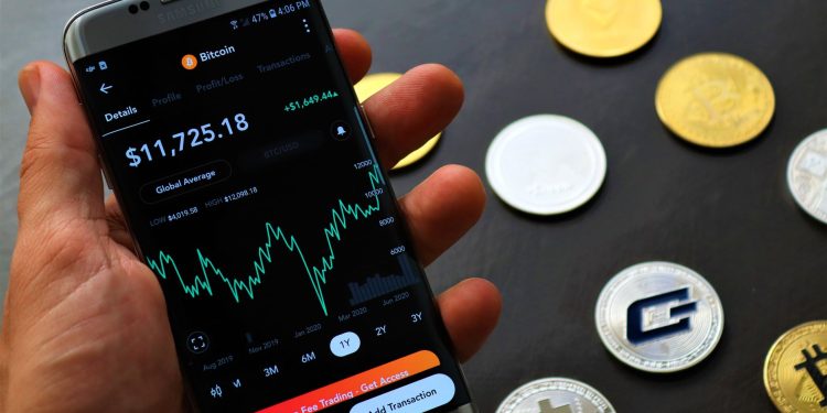 Close-up of a smartphone app showing Bitcoin trading details with crypto coins on a black surface.