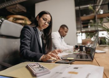 Two business professionals collaborating with a laptop and calculator in a modern office.