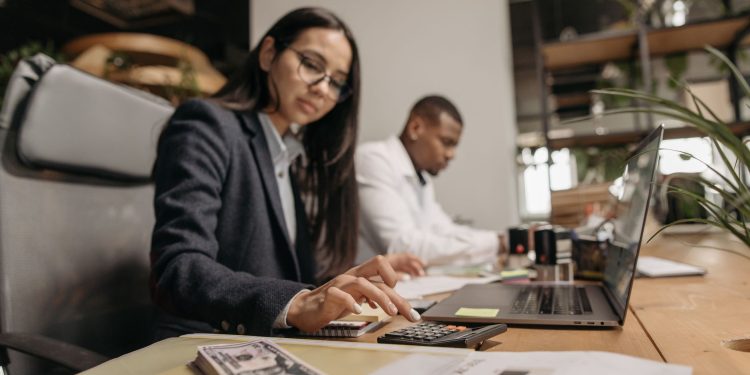 Two business professionals collaborating with a laptop and calculator in a modern office.