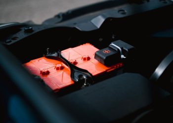 Detailed view of an orange car battery inside a vehicle's engine bay, highlighting its features.