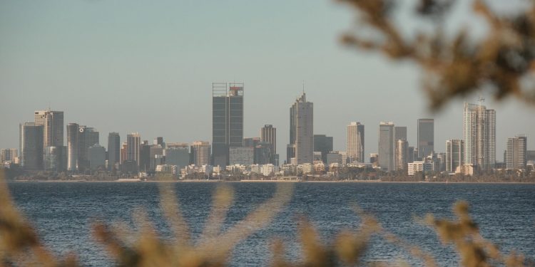 View of Perth skyline across water framed by foliage with a calm atmosphere at dusk.