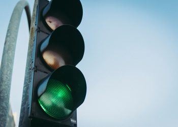 Close-up of a green traffic light against a clear blue sky, symbolizing go and safety.