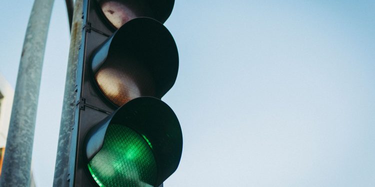 Close-up of a green traffic light against a clear blue sky, symbolizing go and safety.