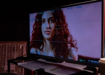 A monitor displays a woman's portrait with technical overlay, indoors.