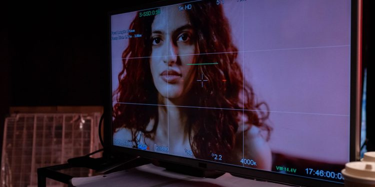 A monitor displays a woman's portrait with technical overlay, indoors.