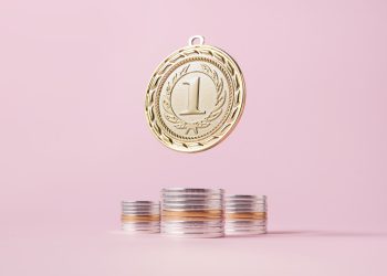 A gold medal and stacks of coins on a light pink backdrop, symbolizing victory and wealth.