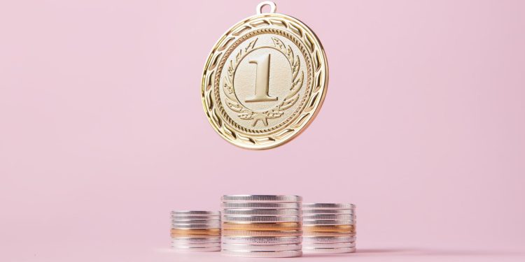 A gold medal and stacks of coins on a light pink backdrop, symbolizing victory and wealth.