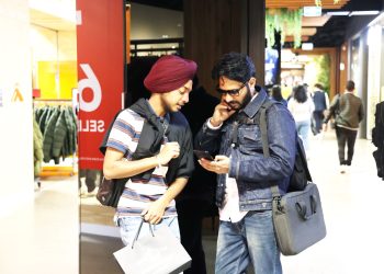 Two men casually shopping and checking a smartphone in a modern mall setting.