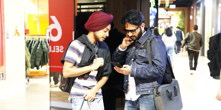 Two men casually shopping and checking a smartphone in a modern mall setting.