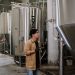 Asian man inspecting stainless steel tanks in a brewery, showcasing modern industrial processes.