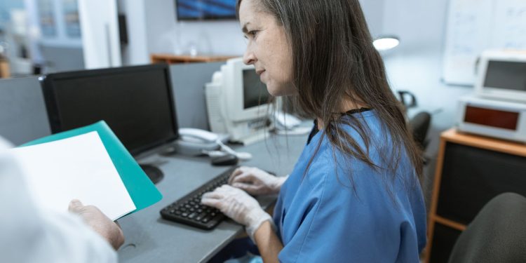 Nurse in scrubs typing on a keyboard at a medical workstation.