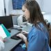 Nurse in scrubs typing on a keyboard at a medical workstation.