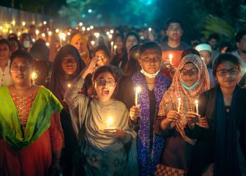 A diverse group of people holding candles at a nighttime vigil outdoors.