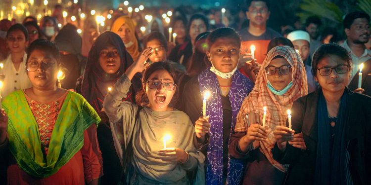 A diverse group of people holding candles at a nighttime vigil outdoors.