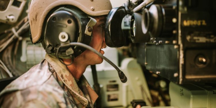 A soldier in uniform operates military equipment inside a vehicle, showcasing modern military technology.