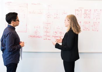 Two professionals brainstorming digital marketing ideas on a whiteboard.