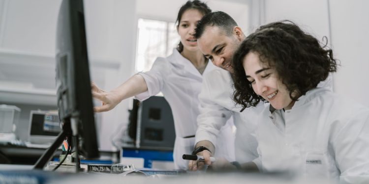Group of diverse scientists working together on a computer in a bright, modern laboratory.