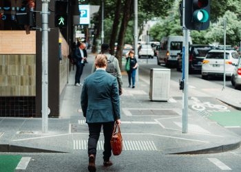 A businessman in a suit crossing the street in a busy urban area during the day.