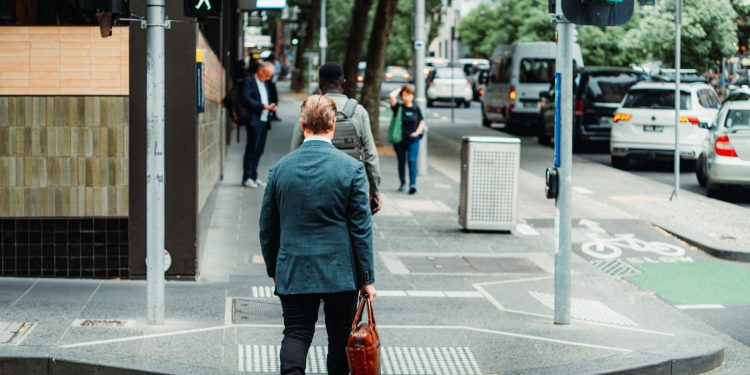 A businessman in a suit crossing the street in a busy urban area during the day.