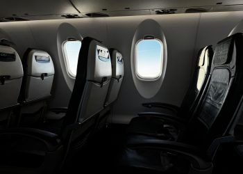 Interior of an empty airplane cabin with a bright sky visible through the window.