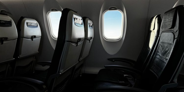 Interior of an empty airplane cabin with a bright sky visible through the window.