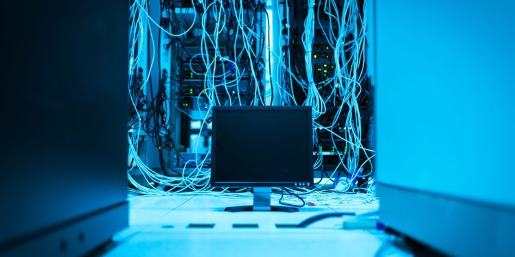 A complex network of cables in a data center with a monitor in the foreground.