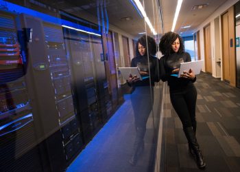 A woman using a laptop navigating a contemporary data center with mirrored servers.