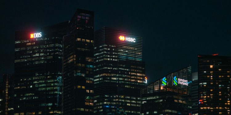 Illuminated city skyscrapers of major banks in Singapore's financial district at night.
