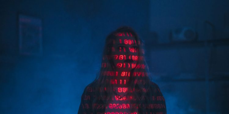 A mysterious silhouette with red binary code projected over the face, set against a dark, moody background.
