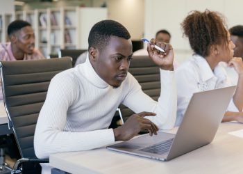 Young man intently working on a laptop in an office setting, concentrating on his task.