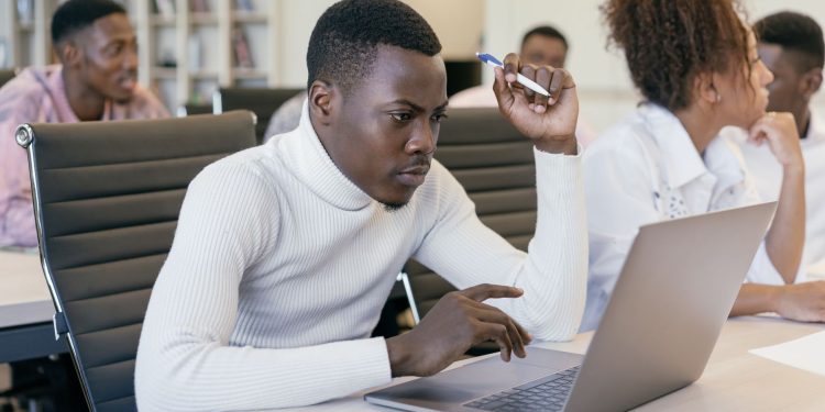 Young man intently working on a laptop in an office setting, concentrating on his task.