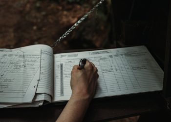 Close-up of a person writing in an outdoor logbook on a table.