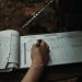 Close-up of a person writing in an outdoor logbook on a table.