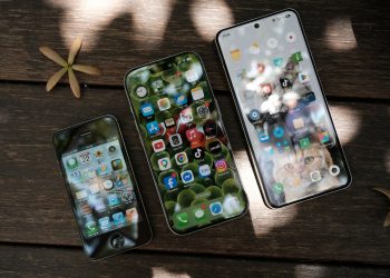 A collection of smartphones showing different app icons, placed on a wooden surface in natural light.