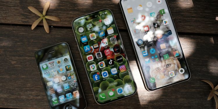 A collection of smartphones showing different app icons, placed on a wooden surface in natural light.