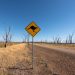 Dirt road in Winton North, Australia with a kangaroo crossing sign and clear blue sky.