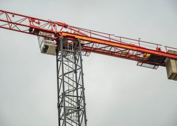 Close-up of a red tower crane against a clear sky, showcasing construction equipment.