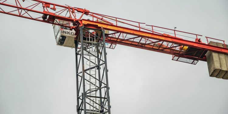 Close-up of a red tower crane against a clear sky, showcasing construction equipment.