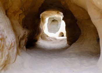 Explore a naturally eroded sandstone tunnel with sunlight filtering through, showcasing intricate geological formations.